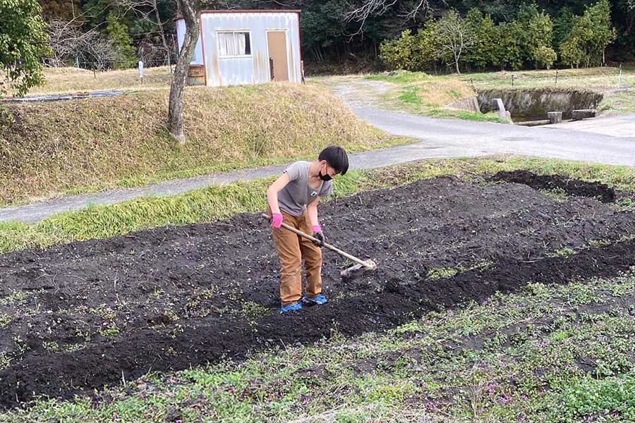 男の子が鍬をもって畑の畝をつくっている