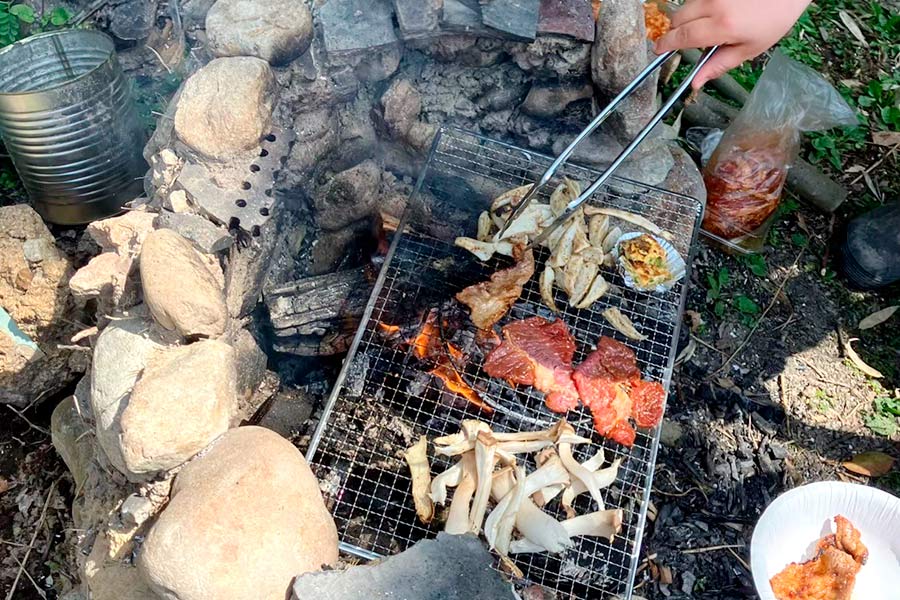 石積みのかまどの中で火を熾して網を張り、肉やキノコを焼いている